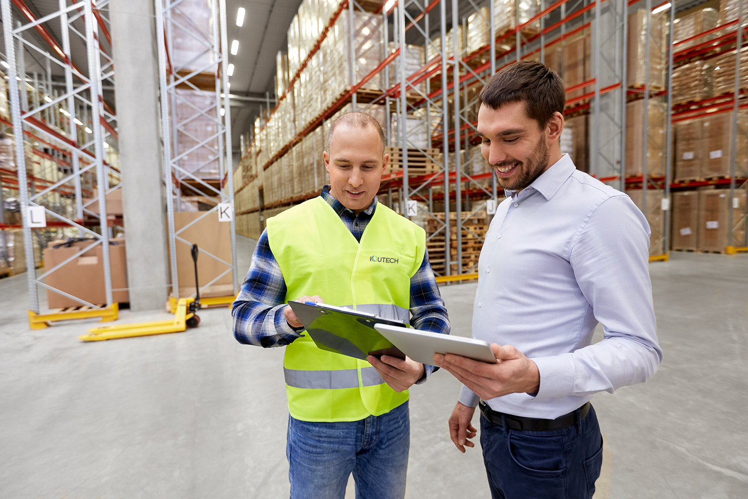 two men check a list in a well-lit warehouse